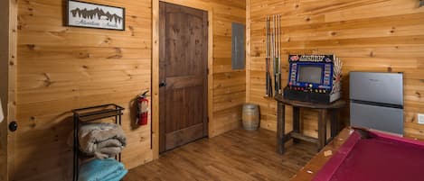 L’intérieur d’un chalet en bois comprend une table de billard, un flipper de la marque Midway, un réfrigérateur et un extincteur.