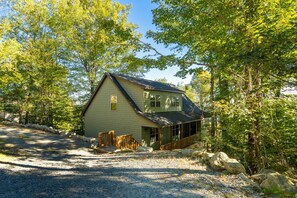 A single-story house with a gabled roof, surrounded by trees and a gravel driveway.