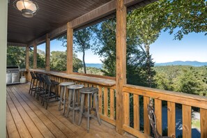 A wooden deck with a bar area, outdoor seating, and a view of the landscape.