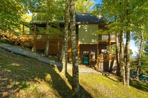 A cabin with a wooden deck, a staircase, and a view of the surrounding forest.