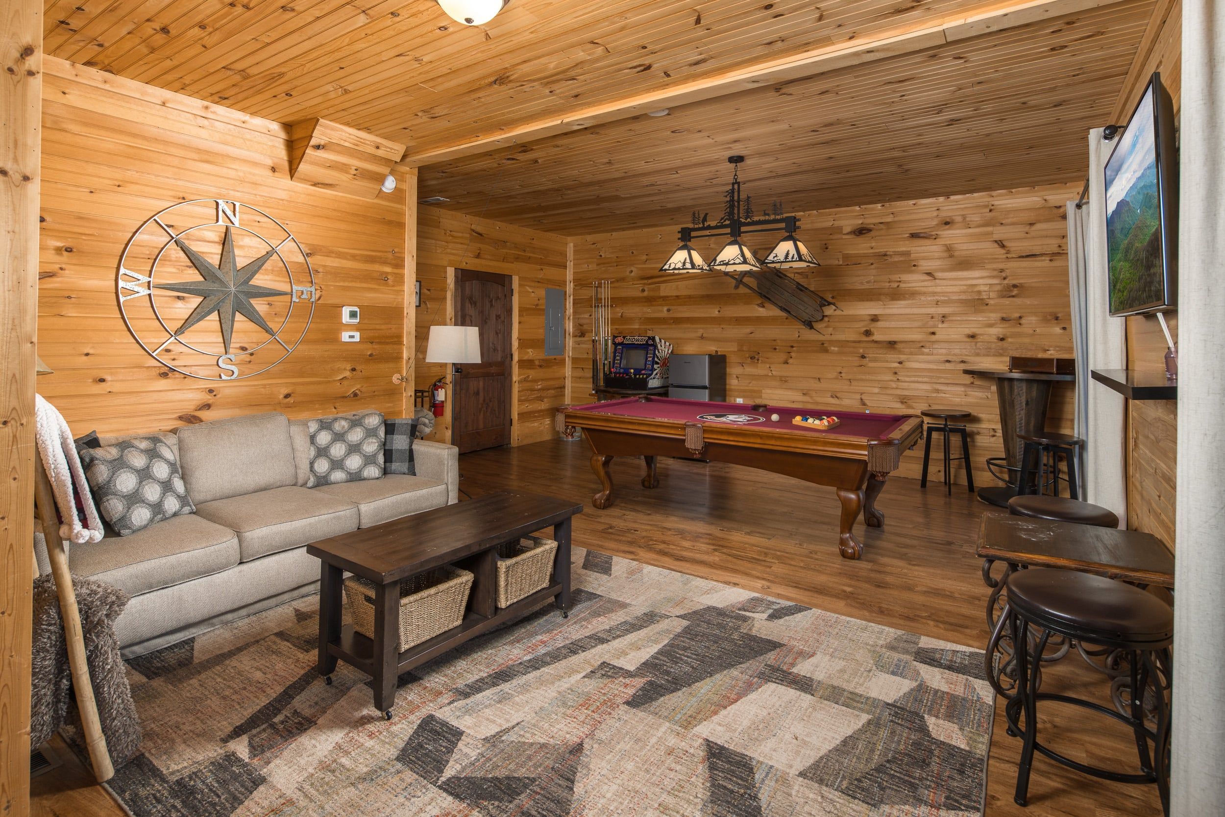 A cozy room with a pool table, a sofa, a coffee table, and a compass wall decoration.
