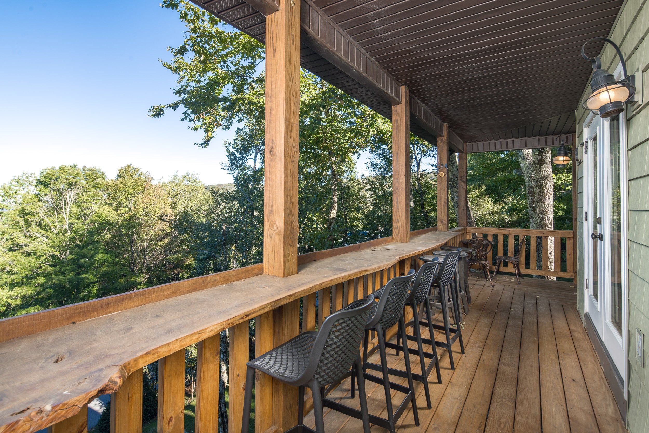 A wooden deck with a covered seating area, featuring a railing and multiple chairs.