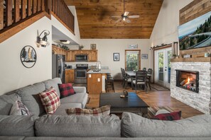 Amplia sala de estar con chimenea, cocina equipada con electrodomésticos modernos y comedor con mobiliario de madera.