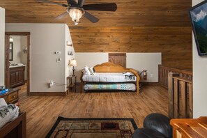 Un dormitorio con techo de madera, una cama con colcha estampada, una mesita de noche con lámpara y suelo de madera.
