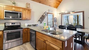 A kitchen with wooden cabinets, stainless steel appliances, a granite countertop, and a dining area with a view. - Walk to Beech Mtn Resort, Sleeps 12, Game Room (Beech Mountain)