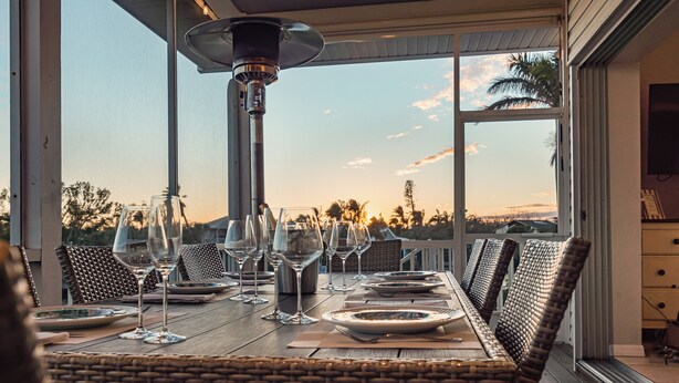 Mesa de comedor para seis personas con sillas de mimbre, una lámpara de mesa y vistas a palmeras y al atardecer.