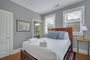 A bedroom with a large bed, a bedside table with a lamp, a mirror, and a window with blinds.