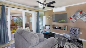 Ein Wohnzimmer mit grauem Sofa, einem gemusterten Sessel, einem Flachbildfernseher und Bildern an der Wand.