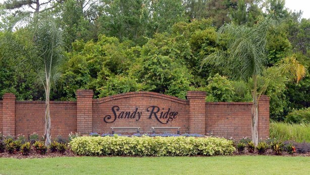 A brick wall with the text "Sandy Ridge" in the center, surrounded by well-maintained landscaping and trees. - Tree Top Retreat (Davenport)