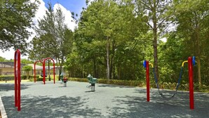 A playground with red and blue play structures, surrounded by trees and a paved area. - Tree Top Retreat (Davenport)