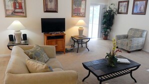 A living room with a sofa, a coffee table, a TV stand, and a chair. There are three paintings on the wall and a ceiling fan. - Tree Top Retreat (Davenport)