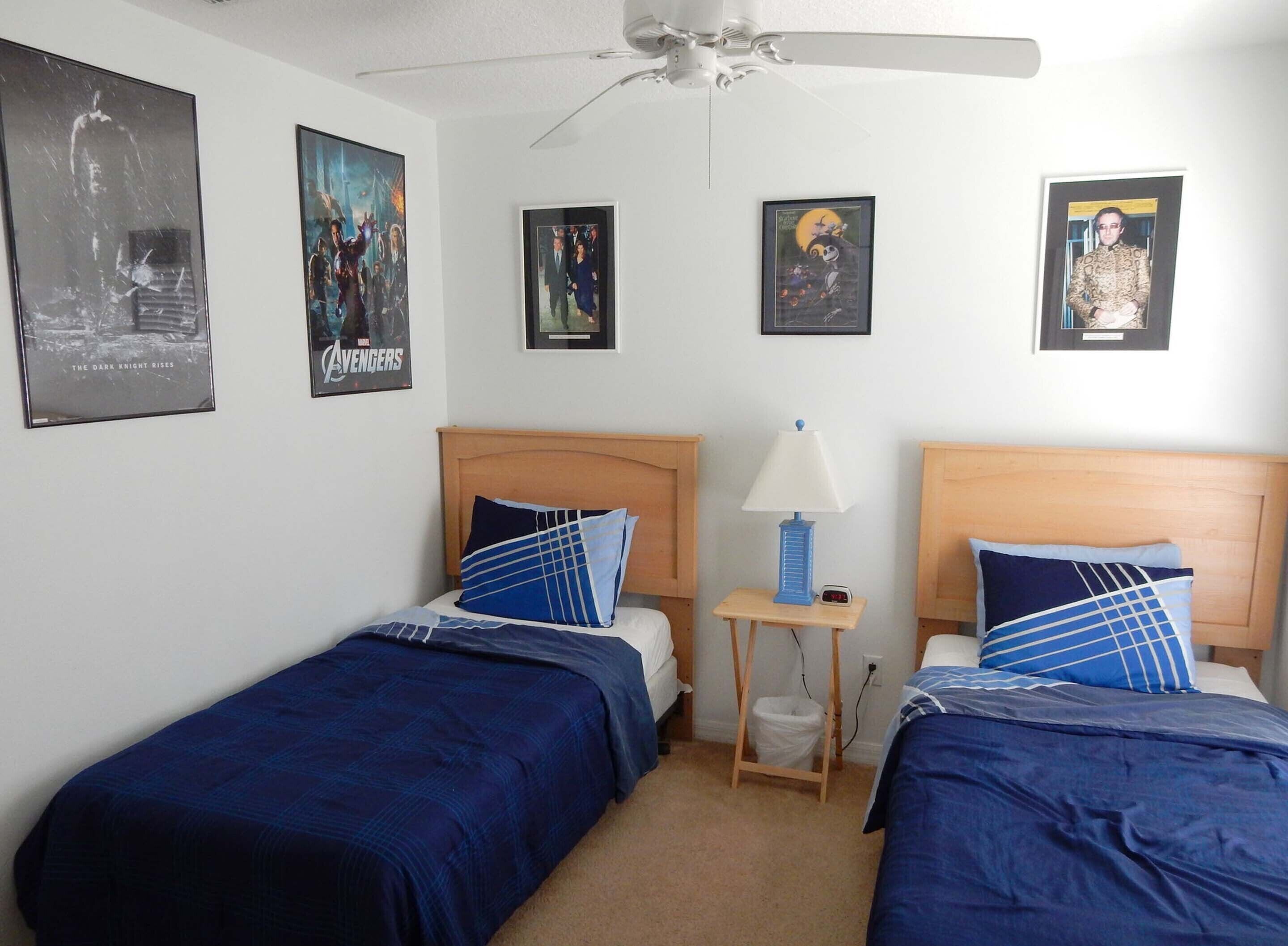 A hotel room with two single beds, a ceiling fan, and posters on the walls.