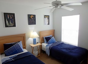 A hotel room with two beds, a ceiling fan, and a window with blinds.