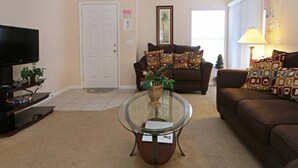 A living room with a television, two sofas, a glass coffee table, and a door.