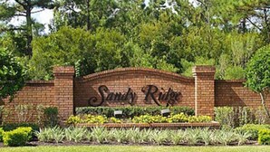 A brick entrance with the sign "Sandy Ridge" surrounded by well-maintained landscaping.