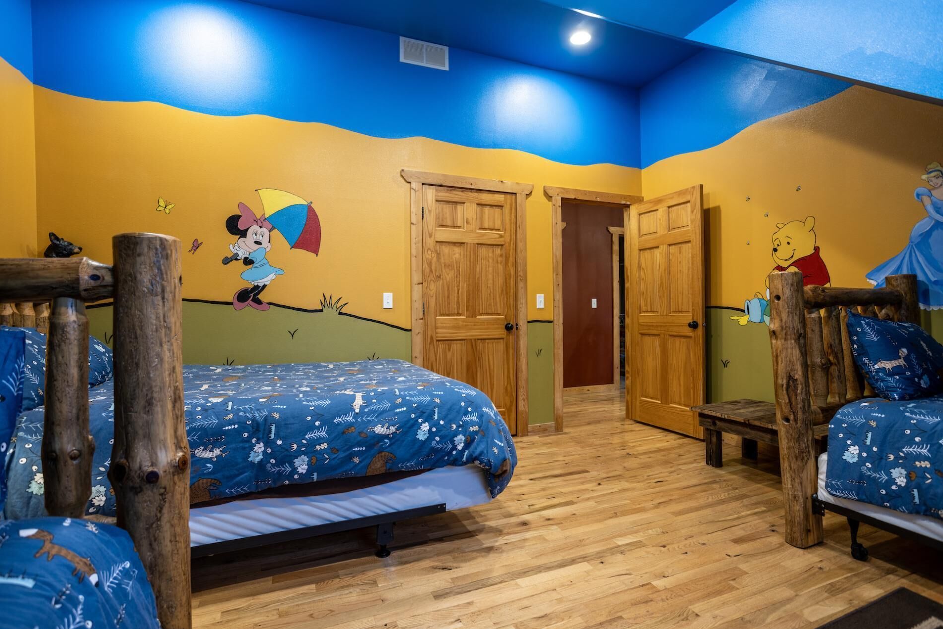 Une chambre avec deux lits, des têtes de lit en bois et une fresque murale représentant un personnage de dessin animé.