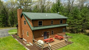 Una baita in legno a due piani con tetto verde, un portico con tavoli da picnic rossi e un camino.