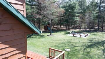 Enjoy the serene surroundings of this cabin's outdoor space, featuring a lawn, deck with seating, and a play structure with a slide.