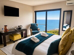 A hotel room with a bed, a desk, a chair, a large window with a view of the sea, and an air conditioning unit. - Aqua Terra (Cape Town)
