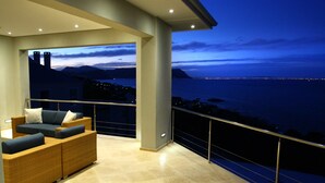 A balcony with a view of the sea and mountains, a sofa, and a railing.