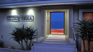 A modern building entrance with a sign reading "AQUA TERRIA" and a view of the ocean through a glass door.