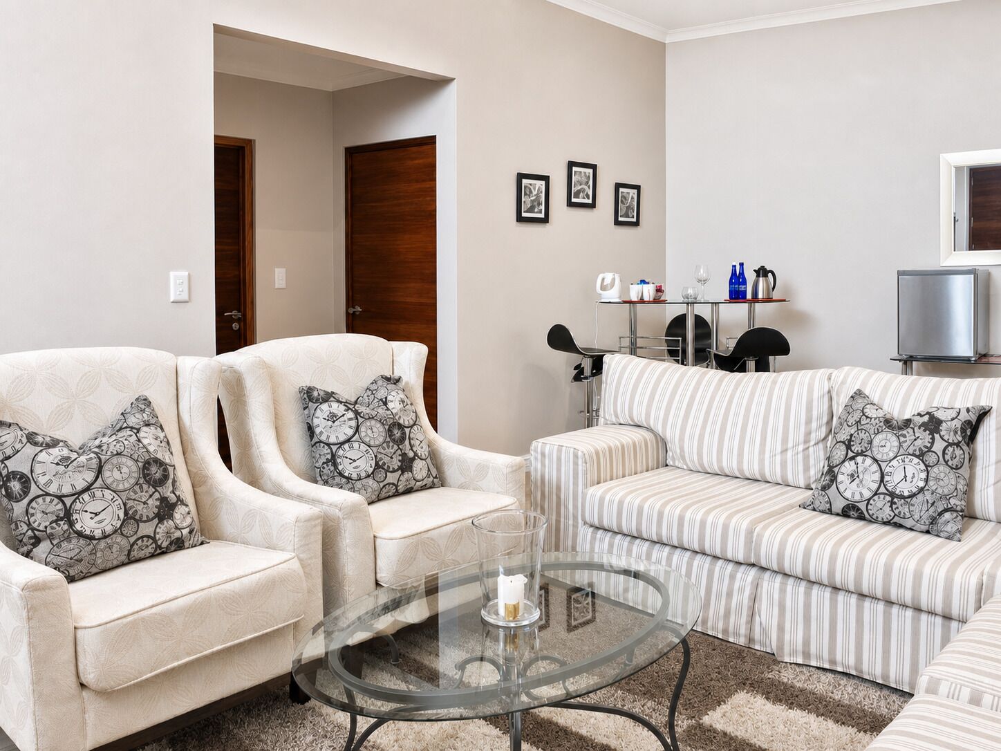 Uma sala de estar com duas poltronas, um sofá, uma mesa de centro de vidro e uma televisão.