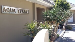 A sign reading "AQUA TERRA" above a building entrance, with large aloe plants in front.
