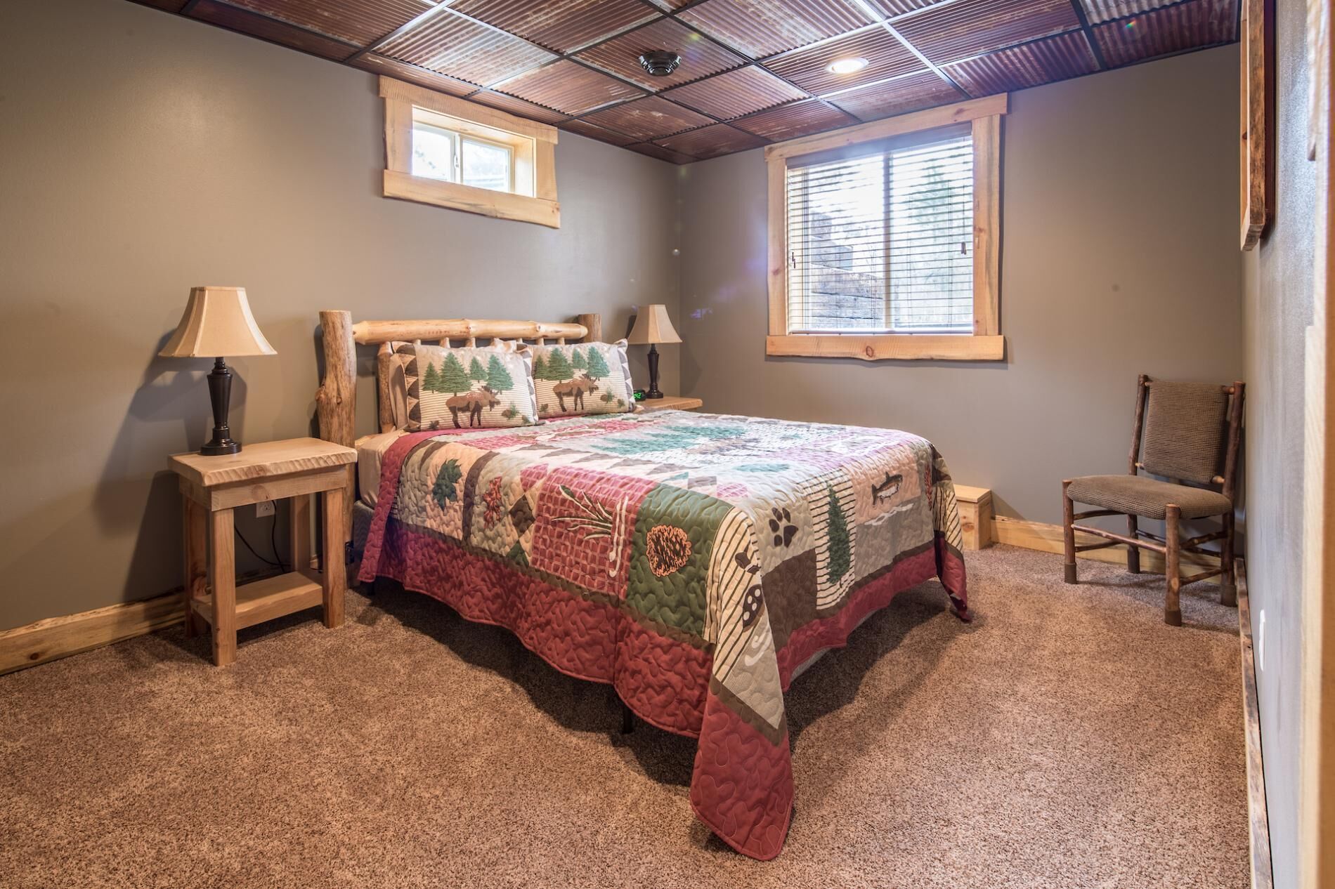 A bedroom with a wooden bed, two bedside tables, a chair, and a window with blinds.