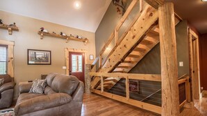 Un salon spacieux avec un escalier en bois, un canapé en cuir et un tableau encadré au mur.