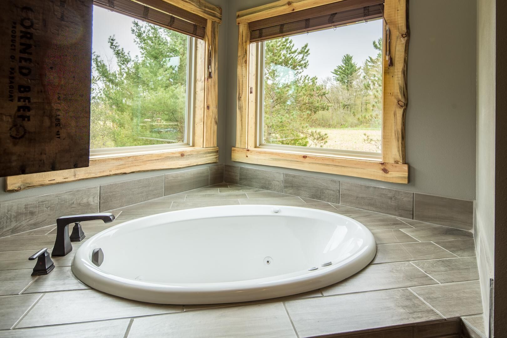 Ein Badezimmer mit freistehender Badewanne, Holzfensterrahmen und Blick auf Bäume und Gras.