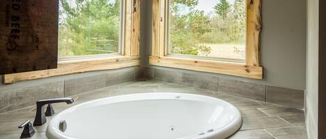 Ein Badezimmer mit freistehender Badewanne, Holzfensterrahmen und Blick auf Bäume und Gras.