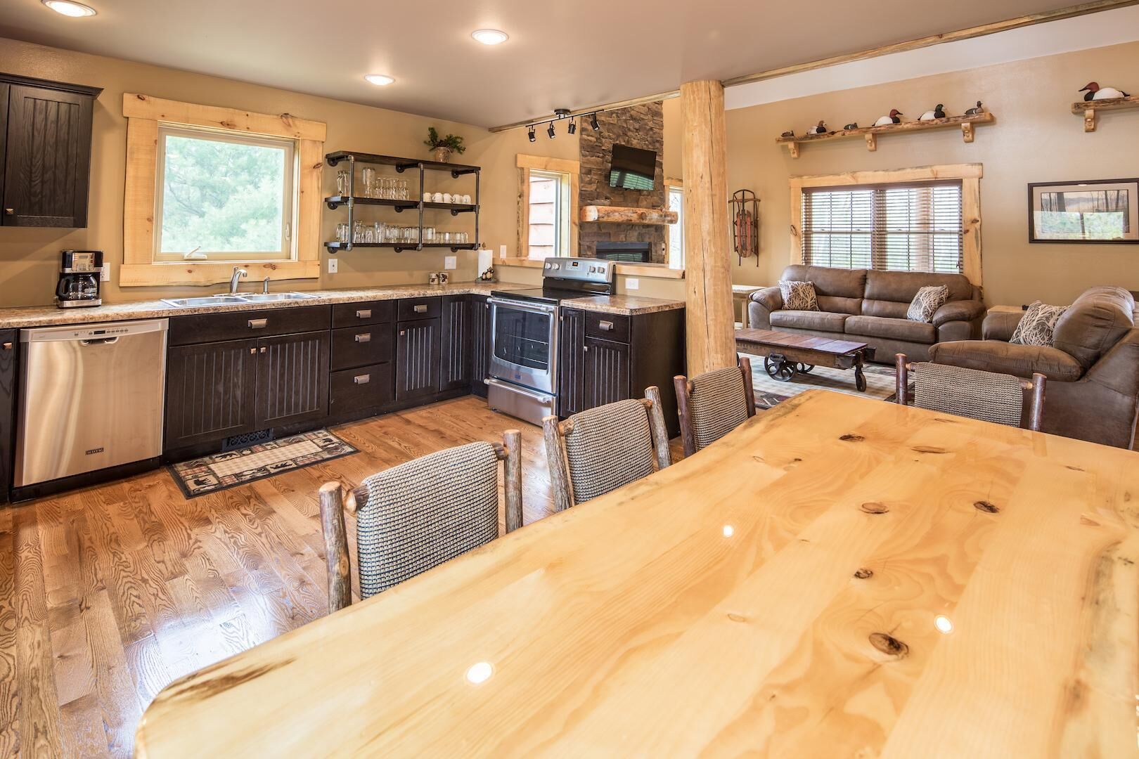 A modern kitchen with dark cabinets, a large wooden table, and a stone fireplace.