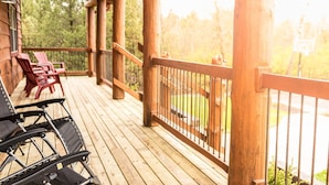 Une terrasse en bois, dotée de chaises et d’un fauteuil roulant, qui offre une vue sur une zone boisée.