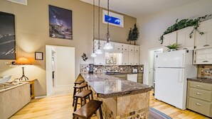 A modern kitchen with a central island, white cabinets, and a tiled backsplash. - Riverfront Hot Tub! Fireplace, Walk to Town (Estes Park)