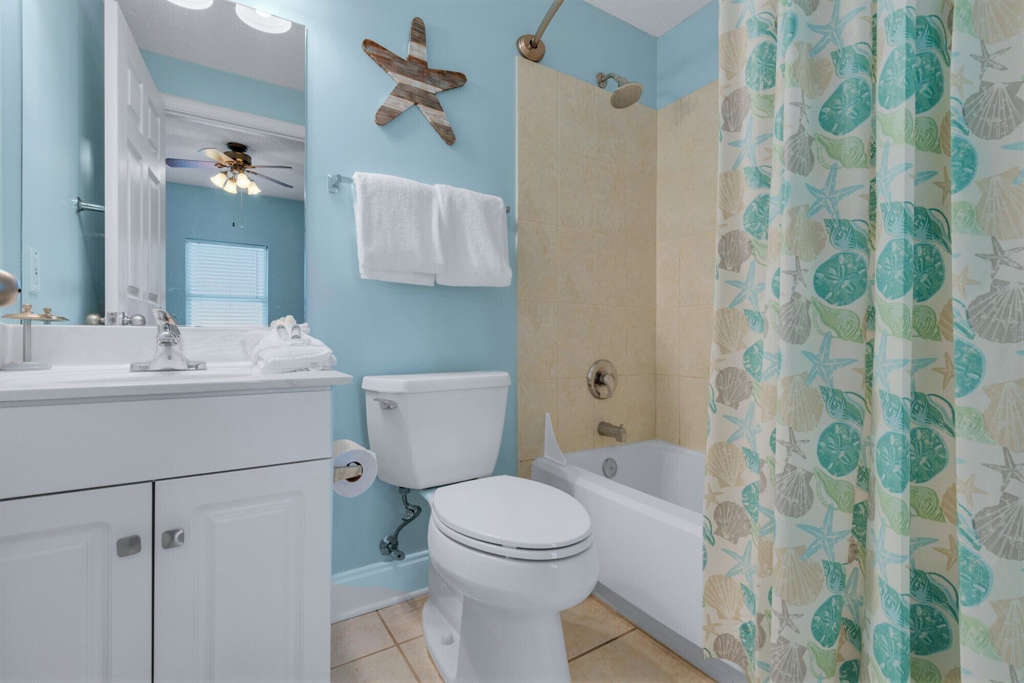 A bathroom with a toilet, sink, and bathtub. There is a starfish decoration on the wall and a shower curtain with a sea shell pattern.