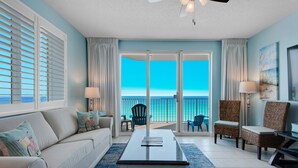 Ein Wohnzimmer mit Sofa, Couchtisch und Sesseln, ein Balkon mit Meerblick und einem Deckenventilator.