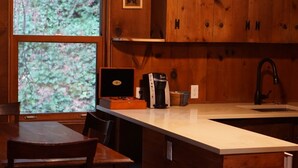 A wooden kitchen with a large window, a coffee maker, and a sink.