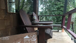A wooden deck with a bench and a table, surrounded by trees.