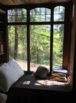 Un coin lecture confortable avec un banc rembourré, un coussin et une pile de livres.