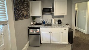 Cocina compacta con armarios blancos, microondas integrado, refrigerador y lavabo.