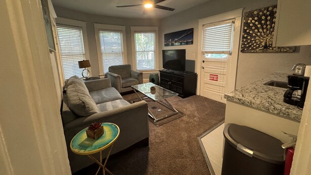 Un espacio habitable compacto con sofá, sillón, mesa de centro, televisor y una pequeña cocina con lavabo y encimera.