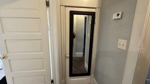 Un pasillo con una puerta blanca, un espejo y un interruptor de luz en la pared.