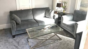 Una sala de estar con un sofá gris, una mesa de centro de vidrio y un sillón gris.