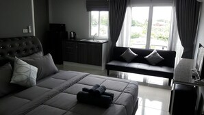 Una habitación de hotel moderna con una cama grande, un sofá, una pequeña cocina y una ventana con cortinas.