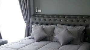 Un dormitorio moderno con una cama grande, cortinas grises y una mesita de noche sencilla.