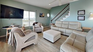 Amplia sala de estar con un televisor de pantalla plana grande, muebles de mimbre, un sofá de cuero color beige y una escalera con barandilla de madera.