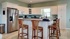 Una cocina con gabinetes blancos, un refrigerador de acero inoxidable, taburetes de bar de madera y una isla grande.