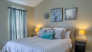 A bedroom with a large bed, two bedside tables with lamps, a window with curtains, and two wall art pieces. - 5 min walk to BEACH (1 block). Newly RENOVATED Spacious 3Beds 3Baths (Gulfport)
