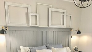 A neatly made bed with a white and blue patterned bedspread, a grey headboard with picture frames, and bedside lamps on either side.