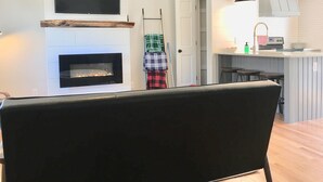 A modern living room with a fireplace, a flat-screen TV, and a dining area with a black chair.